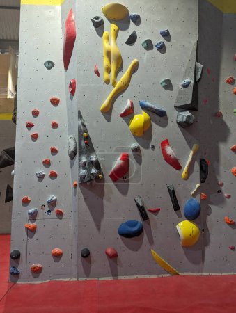 Indoor rock climbing wall featuring colorful climbing holds in a gym setting. Suitable for fitness, exercise, and recreation activities.