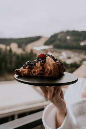 Téléchargez les photos : Une femme en peignoir blanc mange un croissant et boit du café dans un hôtel en montagne. - en image libre de droit