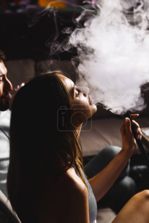 Téléchargez les photos : Un couple amoureux boit un cocktail et fume un narguilé sur la terrasse la nuit. Concept de vie nocturne - en image libre de droit