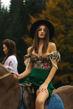 Téléchargez les photos : Les jeunes femmes montent à cheval dans des robes ukrainiennes nationales dans les montagnes des Carpates. Séance photo avec des chevaux dans les montagnes. Concept de culture ukrainienne - en image libre de droit
