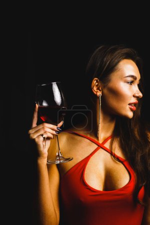 Téléchargez les photos : Un verre de vin rouge dans les mains d'une femme sexy dans une robe rouge - en image libre de droit