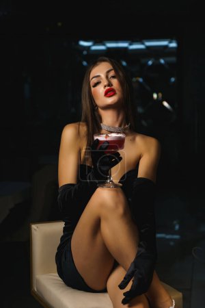 Téléchargez les photos : Femme sexy dans une robe noire avec des gants et des lèvres rouges tient un cocktail.Nightlife concept - en image libre de droit