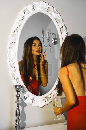 Téléchargez les photos : Femme sexy avec une coupe de champagne dans une robe rouge posant dans une chambre d'hôtel. Concept de vacances coûteux - en image libre de droit