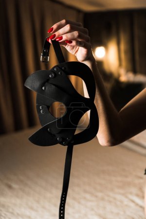 Sexy Frau in schwarzen Dessous posiert mit BDSM Accessoires. Peitsche, Handschellen, Maske. BDSM-Konzept