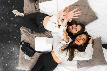 Deux jeunes femmes partagent le bonheur et prennent un selfie au lit dans la chambre. Concept vacances hôtel