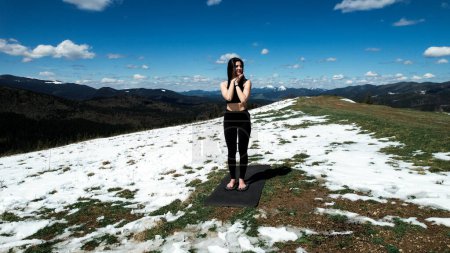 Eine Frau macht Yoga und meditiert an einem sonnigen Tag hoch oben in den schneebedeckten Bergen. Das Konzept von Yoga und Meditation. Sorge um die psychische Gesundheit