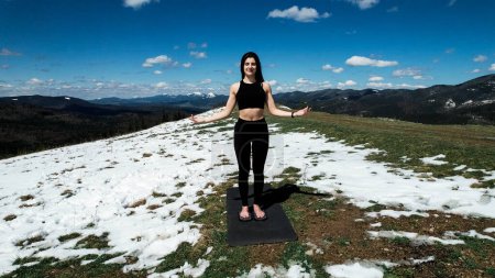 Eine Frau macht Yoga und meditiert an einem sonnigen Tag hoch oben in den schneebedeckten Bergen. Das Konzept von Yoga und Meditation. Sorge um die psychische Gesundheit