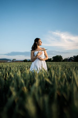 Beautiful woman in a white dress posing and dancing in a green wheat field. Freedom concept.Photo session in a green wheat field