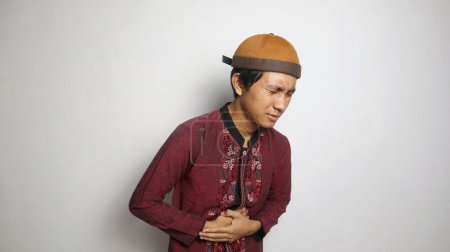Asiatischer muslimischer Mann gestikuliert mit Bauchschmerzen auf weißem Hintergrund