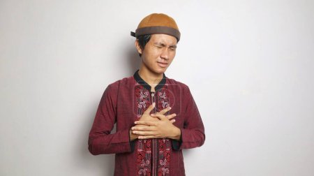 Asiatischer Muslim gestikuliert mit Brustschmerzen auf weißem Hintergrund