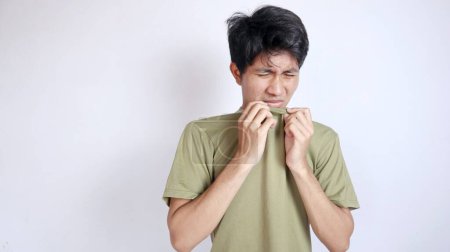Asian man gestures to smell very bad body odor on an isolated white background