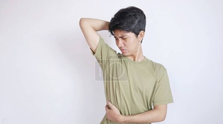 Asian man gestures to smell very unpleasant body odor in his armpit on an isolated white background