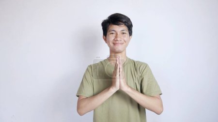 Primer plano del guapo hombre asiático sonriendo con gesto de saludo sobre un fondo blanco aislado