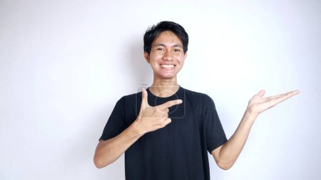 joven asiático hombre sonriendo gesto derecho apuntando izquierda palma en aislado blanco fondo