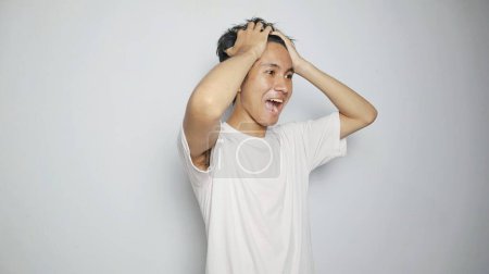 Téléchargez les photos : Jeune homme asiatique en chemise blanche gesticulant avec la main tenant la tête, se sentant étourdi, malade, stressé, déprimé sur fond blanc isolé - en image libre de droit
