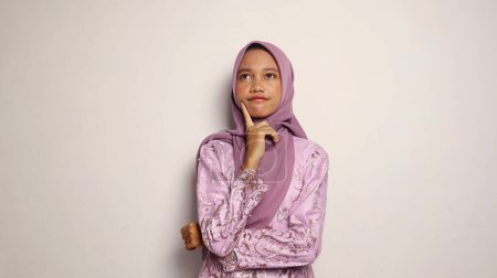 Asian teenage girls dressed in kebaya and hijab pose thinking on an isolated white background