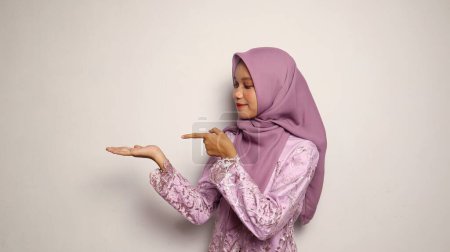 Adolescentes indonesias con kebaya y gesto de hiyab señalando sus palmas sobre un fondo blanco aislado
