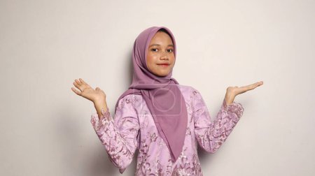 Indonesische Teenager-Mädchen mit Kebaya und Hijab-Geste, die offene Handflächen auf einem isolierten weißen Hintergrund zeigen