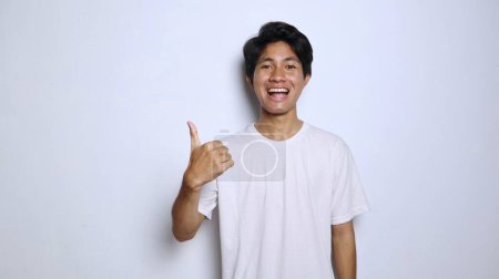 aufgeregter junger asiatischer Mann in weißem Hemd mit lustigem Gesichtsausdruck, Daumen hoch okay, toll, cool, stetig, gewinnend isoliert weißer Hintergrund