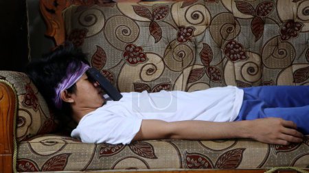 joven asiático hombre durmiendo en sofá con smartphone en su cara