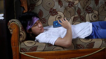 joven asiático hombre dormido en sofá y holding smartphone