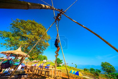 Téléchargez les photos : CHIANG RAI, THAILAND - December 14, 2019 - Hill tribe boy is playing wooden swing at Doi Sa Ngo viewpoint, Chiang Rai province. - en image libre de droit