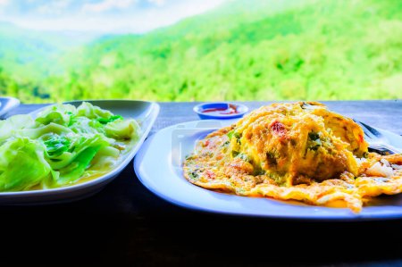 Thai traditional minced pork omelette with rice and stir fried cabbage with fish sauce amidst the refreshing mountain atmosphere, Thailand.