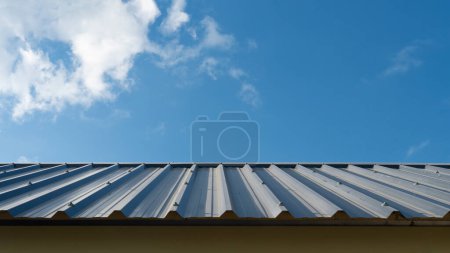 Foto de Lámina metálica de techo azul dispuesta en el techo. Techo de la cadera de la casa está bellamente forrado. Construcción de una casa bajo el cielo azul y nubes blancas. - Imagen libre de derechos