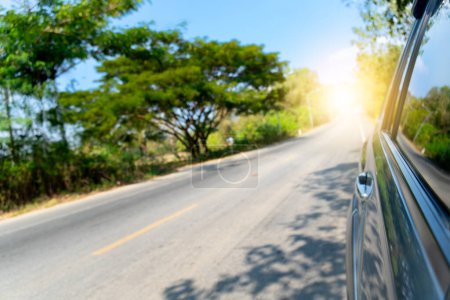 Photo for View on the side of car showing the windows and shiny light of car. Driving on asphalt road the side with nature of green trees. light coming straight from the destination. - Royalty Free Image