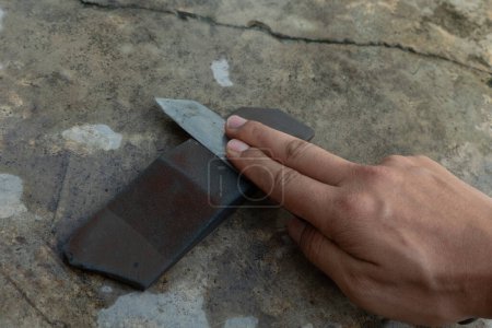 Photo for Knife sharpening on knife sharpening stone. Background of cement floor and hand holding knife sharpening. - Royalty Free Image