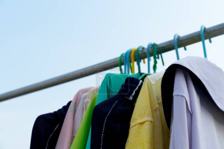 Téléchargez les photos : Des vêtements colorés suspendus avec des cintres. Cintre à vêtements accroché à une rampe de fer. sous le ciel clair. - en image libre de droit
