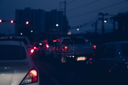 Photo for Rear side of white car at night with turn on brake light on the road. Traffic jam at nigth time. Cars lined up on the road in urgent traffic condition. Tall buildings in the distance for background. - Royalty Free Image