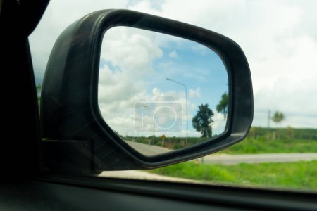 Ala de espejo abstracta del coche. Mirando hacia atrás para viajar con meandros pradera verde bajo el cielo azul. en carreteras sin coches.