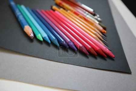 Foto von Buntstiften in einem Farbverlauf angeordnet. Verschiedene Blautöne, rosa Farben. Im Hintergrund defokussierte Gelb- und Rottöne. Kunstmaterialien. Schwarzer und grauer Hintergrund. In einer Reihe angeordnet.