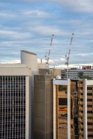 Téléchargez les photos : Vue aérienne des grues de chantier contre un ciel bleu nuageux au premier plan des gratte-ciel imposants d'une ville industrielle, créant un paysage urbain - en image libre de droit