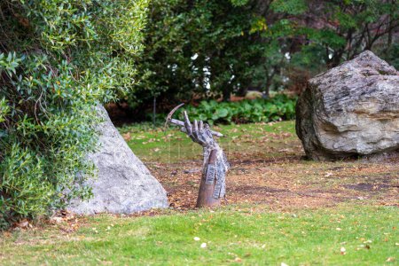 Téléchargez les photos : Queenstown, Nouvelle-Zélande - 13 mai 2023. Sculpture surréaliste d'une main métallique tenant une pioche tranchante soulevée du sol. Mémorial Bruce Grant, situé près de gros rochers dans Queenstown Gardens. - en image libre de droit