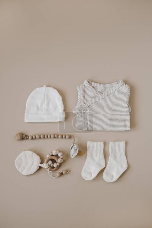 Téléchargez les photos : Cozy vêtements hygge et accessoires pour nouveau-né. Combinaison de base, chaussettes, chapeau, porte-sucette sur fond beige pastel. Collage esthétique minimaliste de mode bébé - en image libre de droit