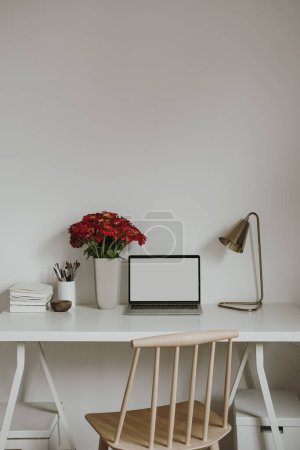 Photo for Laptop computer with blank copy space display on table with stationery, flowers bouquet, lamp. Aesthetic minimalist home office workspace. Mockup template - Royalty Free Image
