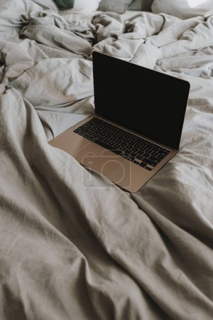 Foto de Ordenador portátil en la cama con ropa de cama arrugada gris. Trabajo en casa, concepto freelance - Imagen libre de derechos