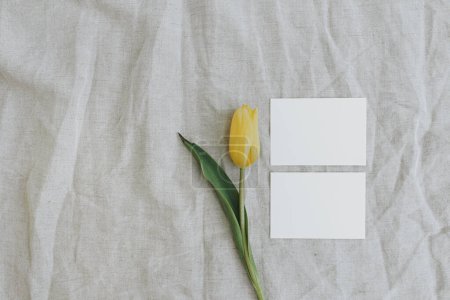 Téléchargez les photos : Cartes d'invitation papier vierges. Fleur de tulipe jaune sur toile de lin froissée neutre. Pose plate, vue du dessus composition florale minimale - en image libre de droit