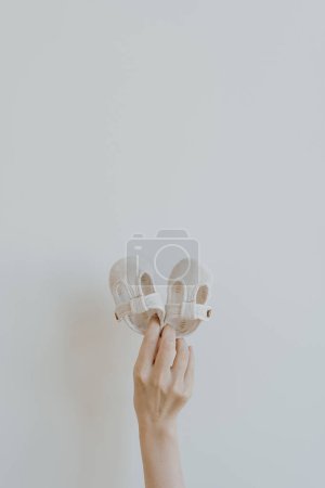 Photo for Person's hands hold cute little baby sandals shoes on white background. Minimalist baby fashion apparel - Royalty Free Image