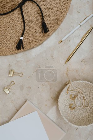 Strohhut, goldene Accessoires auf Marmortisch mit leeren Kopierattrappen. Stilvolle Mode flache Lage, von oben betrachtet minimalistische Arbeitsplatzvorlage für Home Office