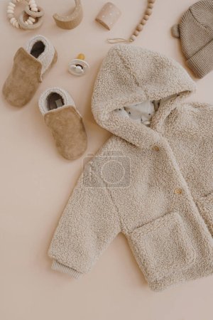 Photo for Warm winter children's jacket, suede booties, hat, pacifier, toys. Baby clothes and accessories set on neutral beige background. Fashion Scandinavian children's clothes. Flat lay, top view. - Royalty Free Image