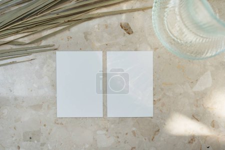 Téléchargez les photos : Carte de feuille de papier vierge avec espace de copie maquette sur la table en marbre. Fond de table en marbre avec silhouette d'ombres de lumière du soleil. Feuille de palmier séchée tige - en image libre de droit