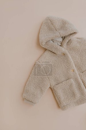 Téléchargez les photos : Veste d'hiver chaude pour enfants. Vêtements bébé sur fond beige neutre. Mode vêtements scandinaves pour enfants. Couché plat, vue du dessus. - en image libre de droit