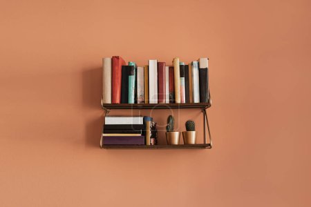 Photo for Books stack on hanging shelf. Coral peach wall background. Aesthetic minimal interior design. Reading, education concept with bookshelf - Royalty Free Image