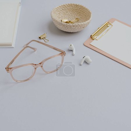 Photo for Clipboard, wireless headphones, glasses, clips in rattan plate. Minimal business copy space template for social media, magazine, blog. Home office desk table workspace - Royalty Free Image