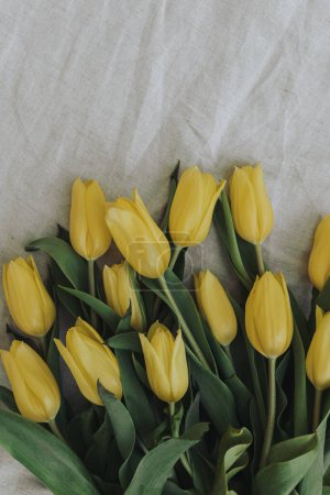 Téléchargez les photos : Délicat bouquet de fleurs de tulipe jaune élégant sur fond de tissu de lin froissé avec espace de copie. Simple esthétique minimaliste pose plate, composition florale vue de dessus - en image libre de droit