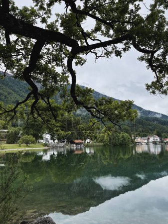 Foto de Pintoresca vista del lago con montañas y reflejos de nubes. Vieja aldea pequeña. Paisaje natural escénico. Vacaciones de verano - Imagen libre de derechos