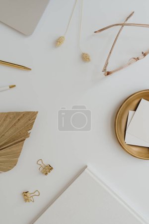 Photo for Home office desk workspace with laptop computer, blank paper card sheet with copyspace, glasses, stationery on white table. Flat lay, top view template. Women's, girl boss work or business background - Royalty Free Image